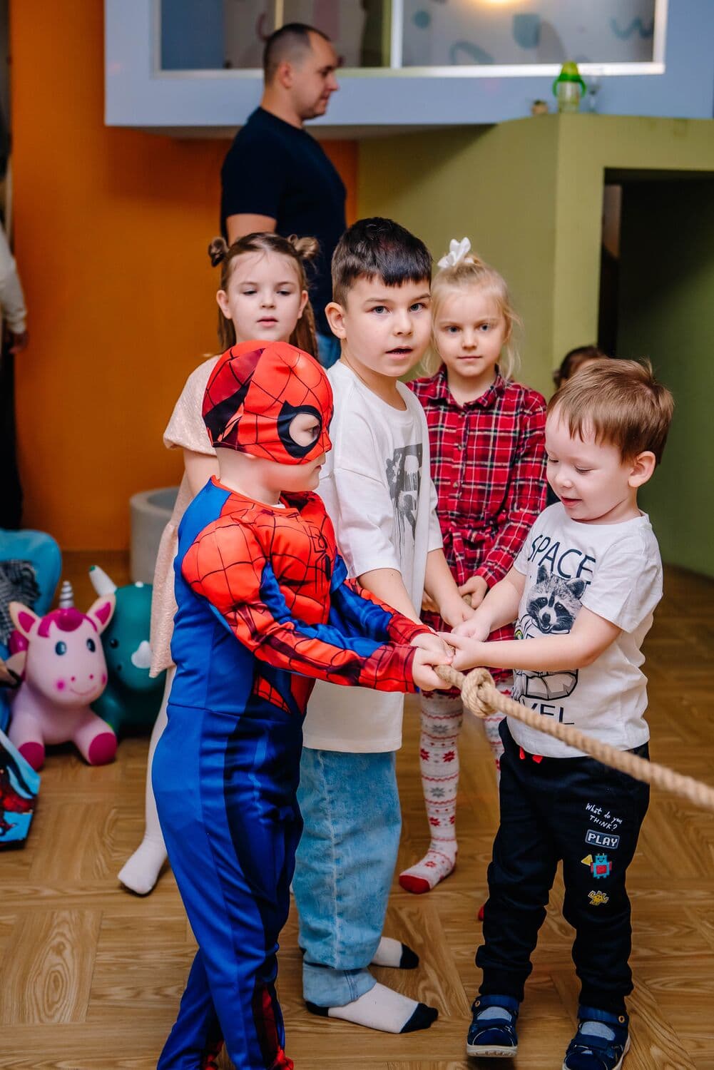 Дети в костюме Человека Паука и в футболках вместе тянут канат